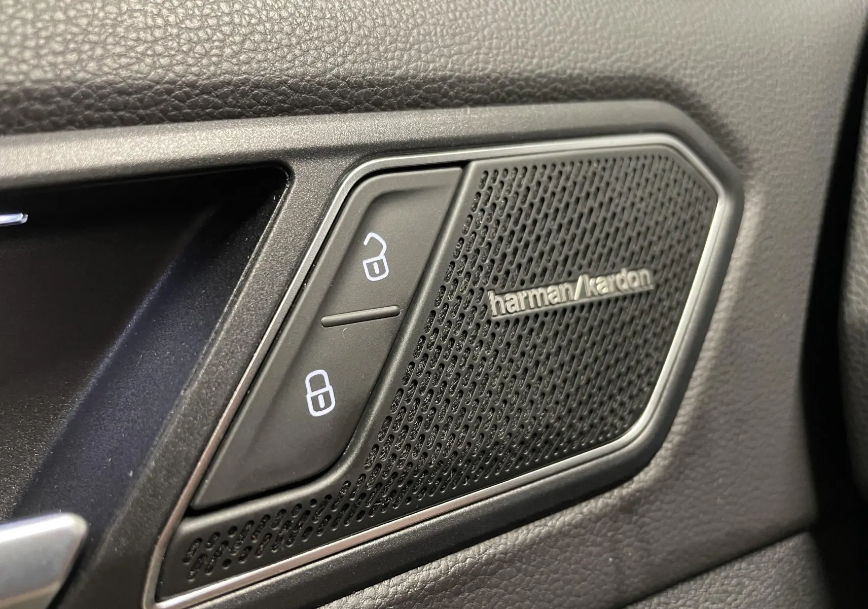Gros plan sur la grille de haut-parleur Harman Kardon et les boutons de verrouillage dans l'habitacle noir du Volkswagen Tiguan.