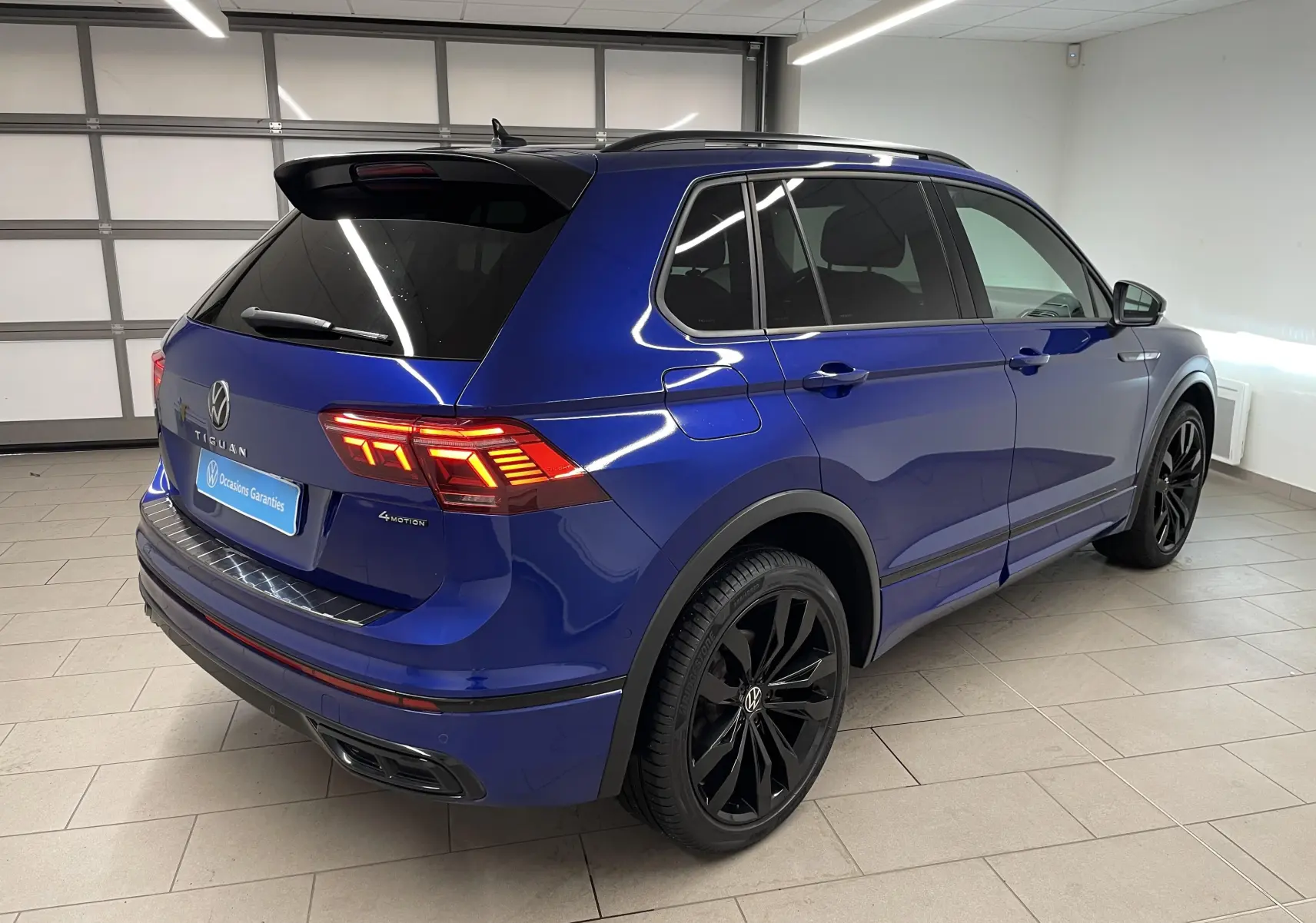 Vue 3/4 arrière droite d'un Volkswagen Tiguan Bleu Lapiz avec jantes noires et vitres arrière surteintées.