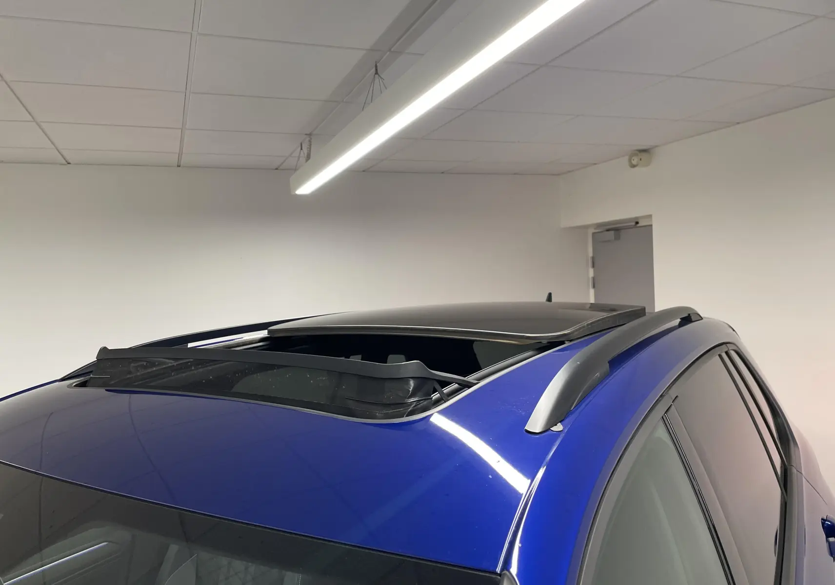 Vue en plongée du toit ouvrant panoramique ouvert sur un Volkswagen Tiguan Bleu Lapiz avec barres de toit grises.