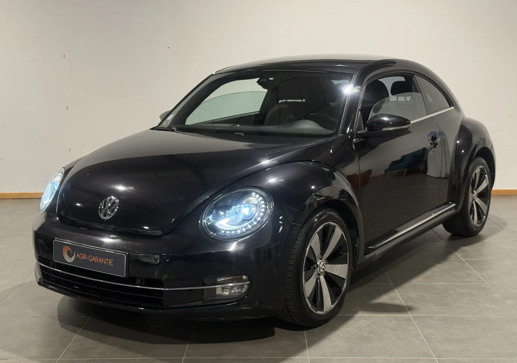 Volkswagen Coccinelle noire 2013 vue 3/4 avant droit avec phares LED allumés et jantes spécifiques Fender Edition.