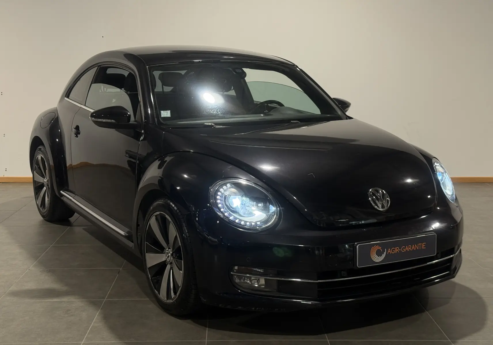 Volkswagen Coccinelle noire 2013 en 3/4 avant droit avec phares LED allumés et jantes spécifiques Fender Edition.