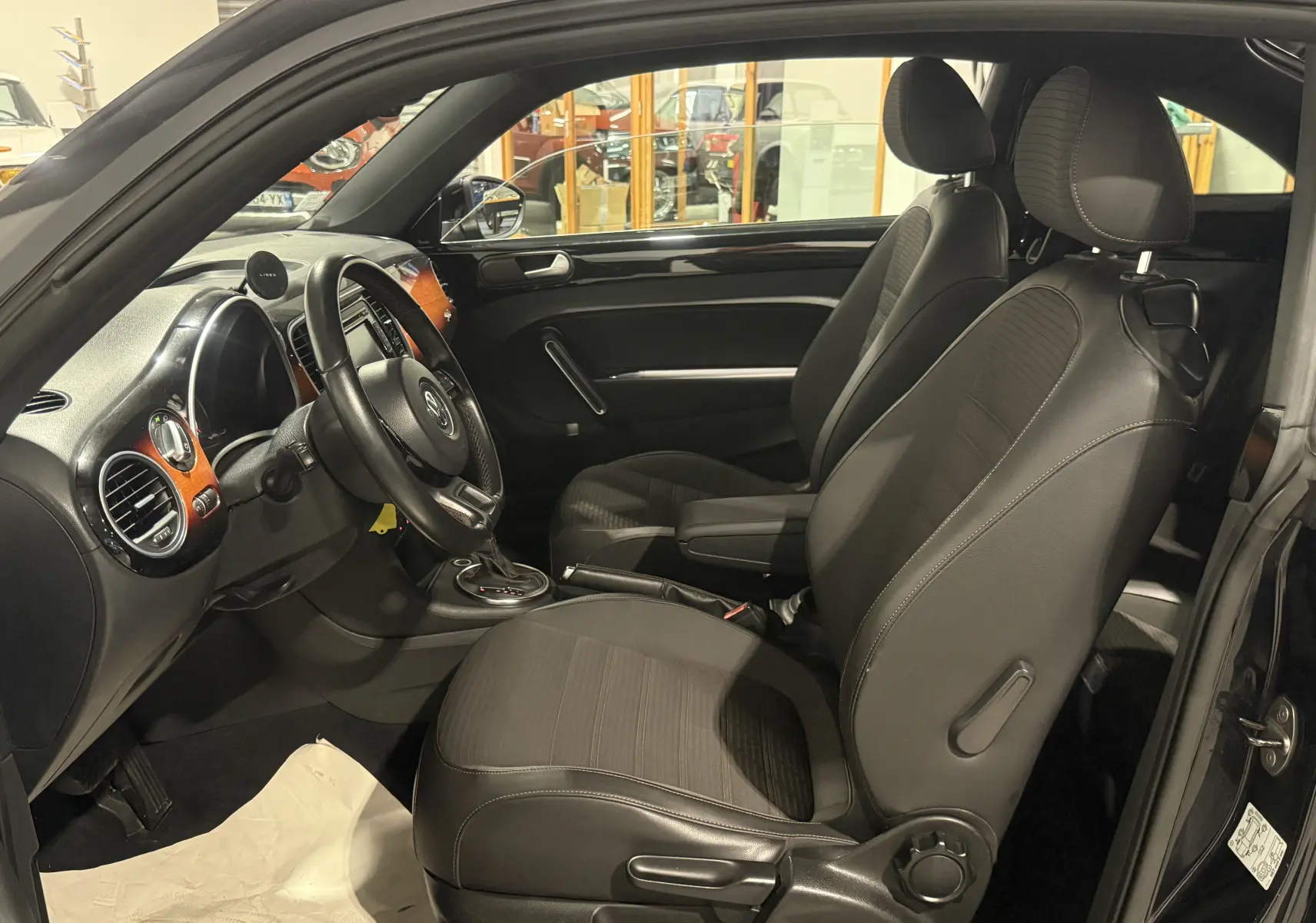 Vue intérieure côté conducteur de la Volkswagen Coccinelle noire 2013 avec sellerie noire et inserts bois sur tableau de bord.