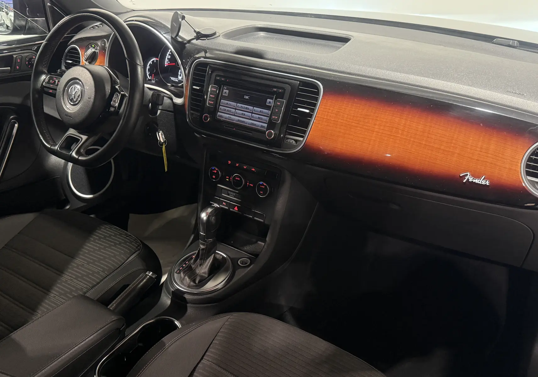 Vue intérieure côté conducteur du Volkswagen Coccinelle noir 2013, tableau de bord avec finition bois Fender et boîte auto.