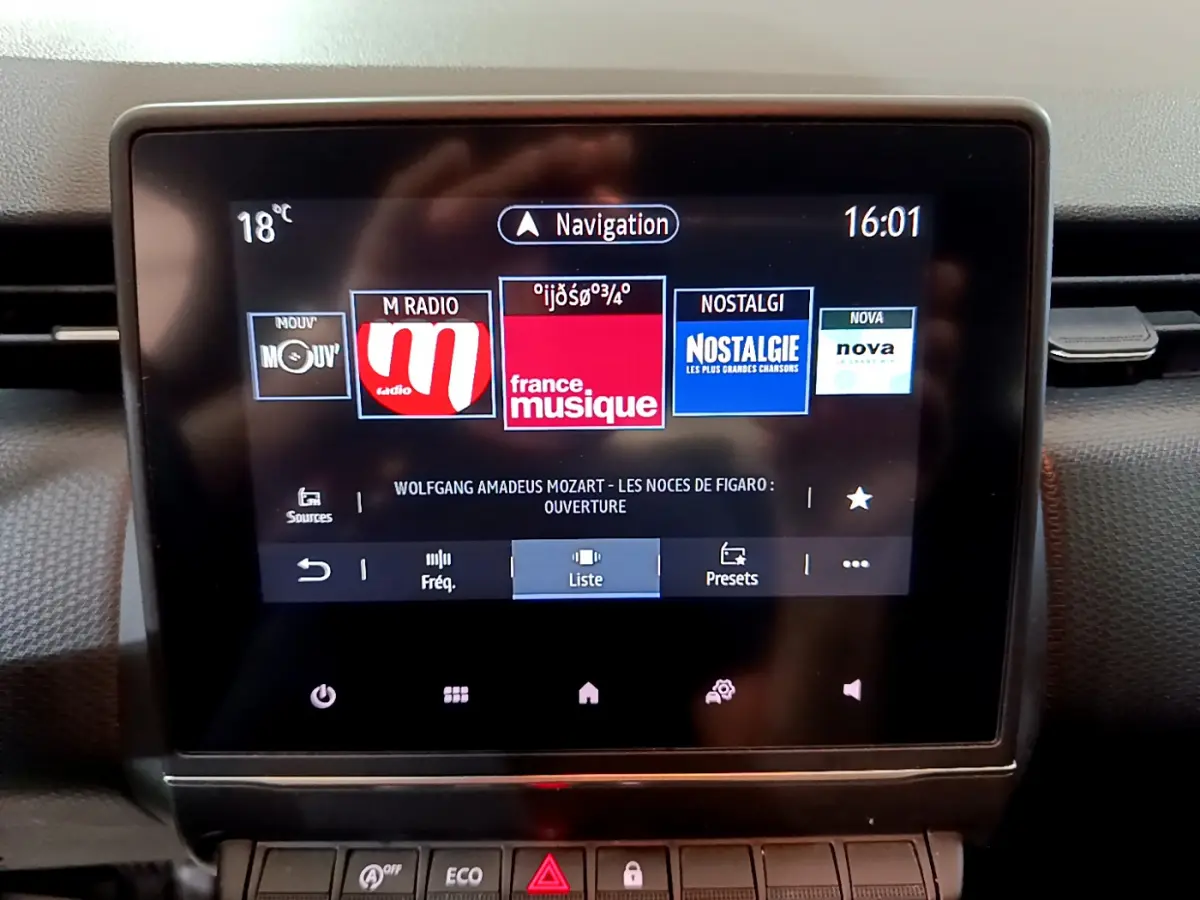 Écran tactile central de la Renault Clio Business blanc, affichant les stations radio et la navigation, vue de face.
