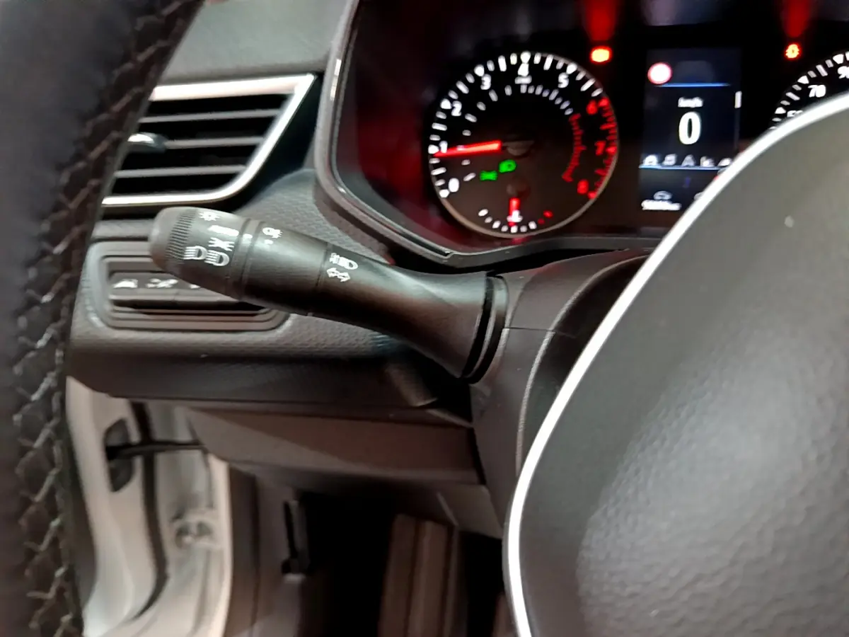 Gros plan sur le commodo gauche et le tableau de bord numérique de la Renault Clio Business TCe 90 blanche de 2021.