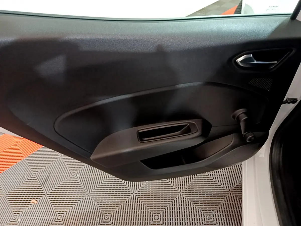 Vue intérieure du panneau de porte côté gauche d'une Renault Clio blanche, avec poignée et commande de vitre manuelle.