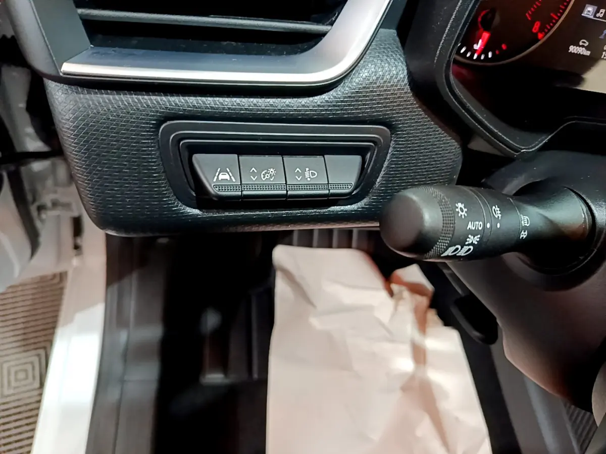 Gros plan sur les commandes d'assistance et réglage des phares côté gauche du tableau de bord d'une Renault Clio blanche.