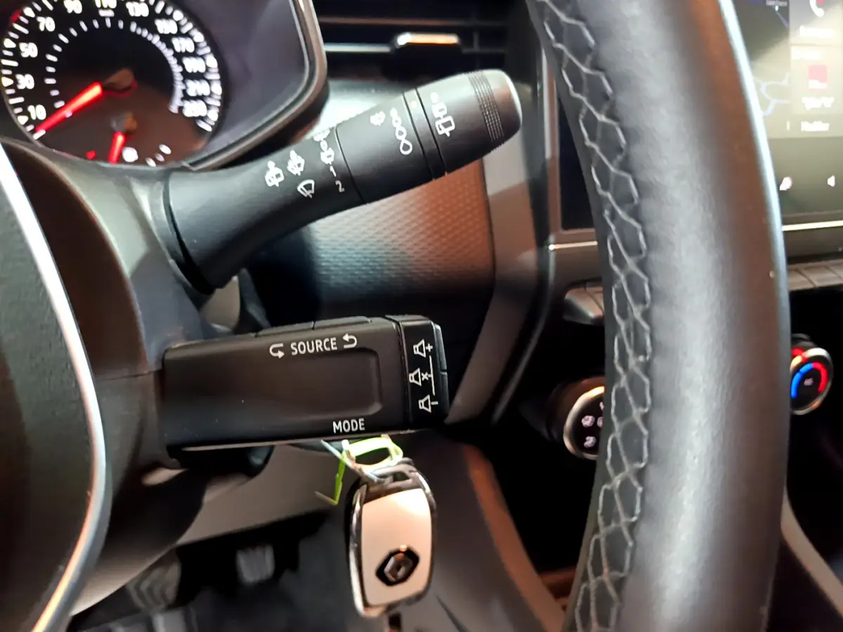 Gros plan sur le volant cuir et les commandes au volant d'une Renault Clio blanche, tableau de bord partiellement visible.