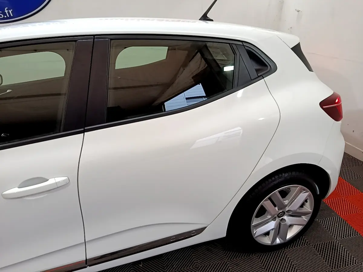 Vue latérale droite d'une Renault Clio Business TCe 90 blanche, mettant en valeur la porte arrière et la roue arrière.
