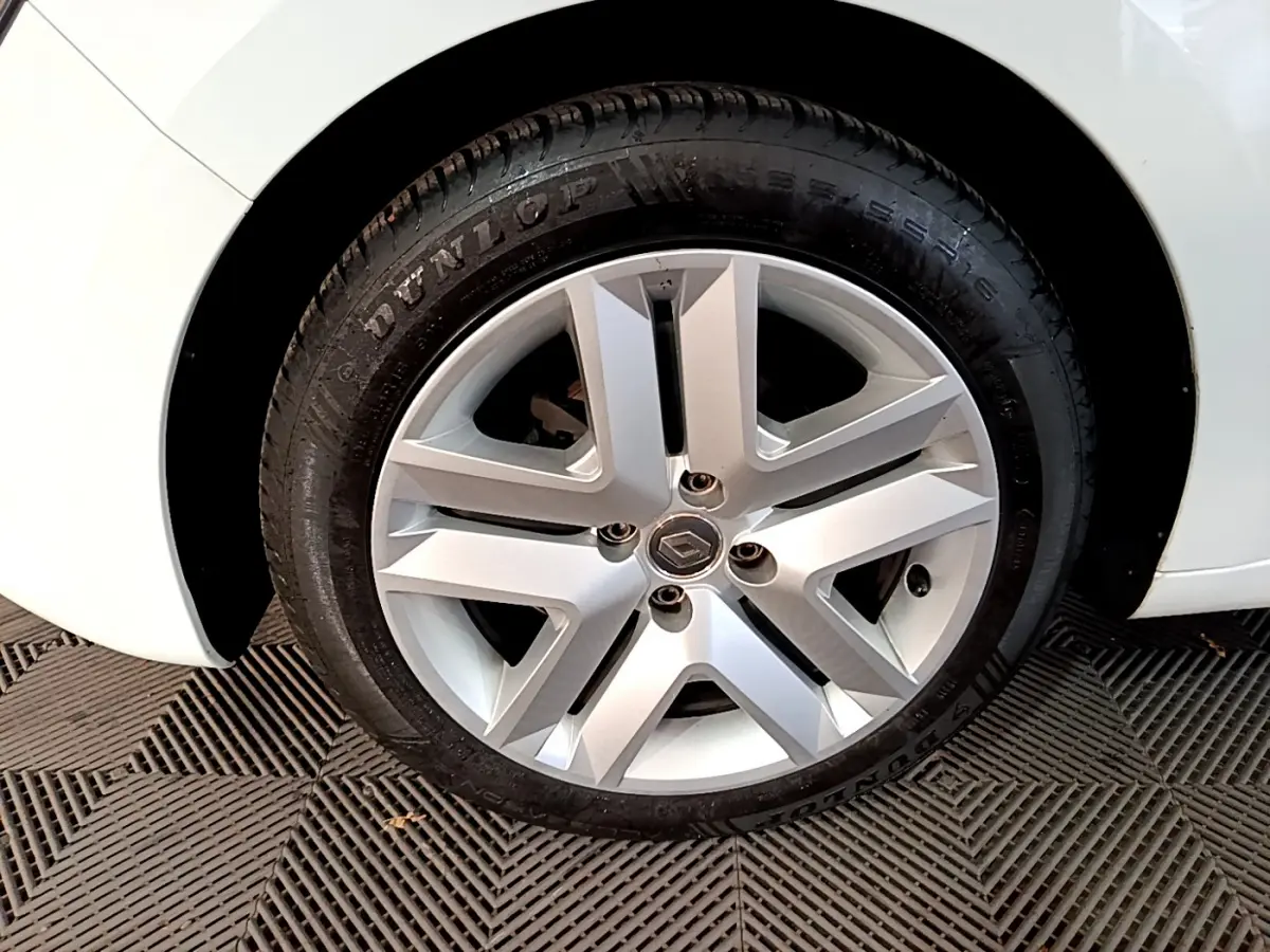 Vue rapprochée de la roue arrière droite d'une Renault Clio Business TCe 90 blanche, sur sol texturé.