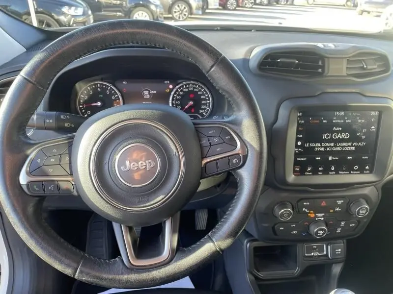 Vue intérieure centrée sur le volant Jeep noir et le tableau de bord avec écran tactile du Renegade blanc de 2019.