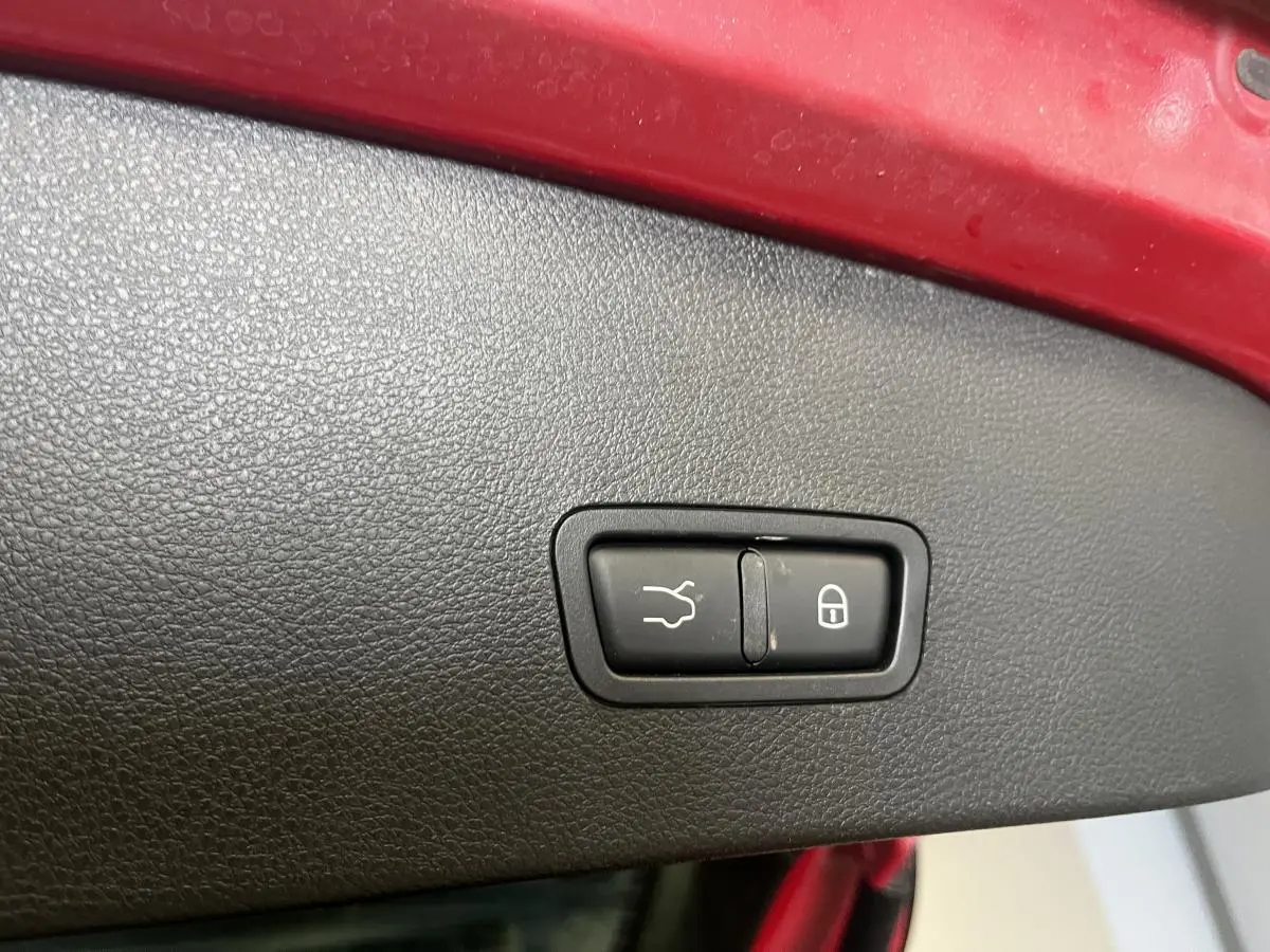 Gros plan sur bouton d’ouverture de coffre et verrouillage, intérieur noir, bord de coffre rouge Alfa Romeo Tonale 2024.