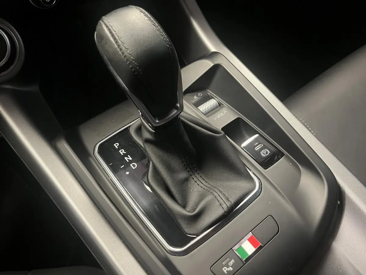 Gros plan sur la console centrale noire de l'Alfa Romeo Tonale avec levier de vitesse automatique et logo tricolore italien.
