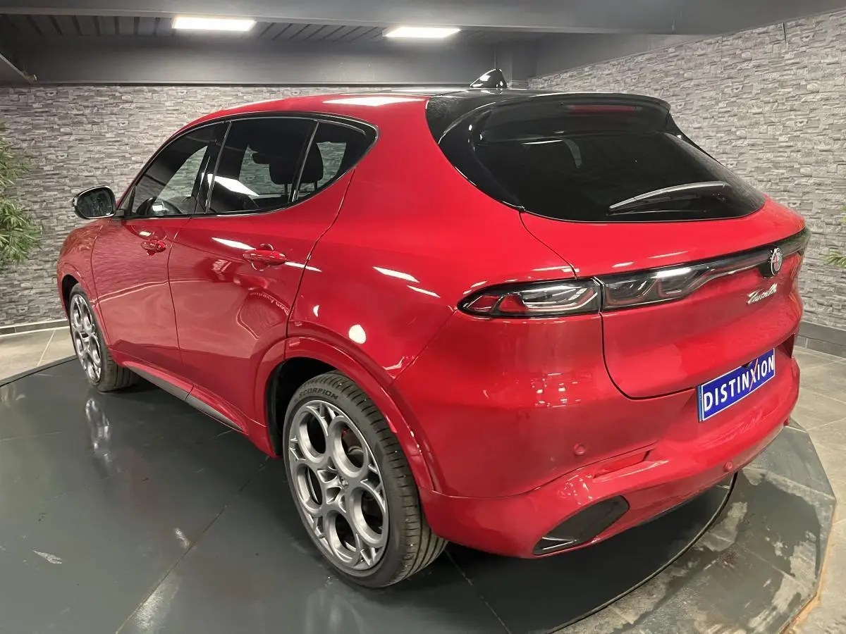 Vue 3/4 arrière droite d'un Alfa Romeo Tonale rouge avec jantes alliage 20 pouces et toit noir en intérieur showroom.