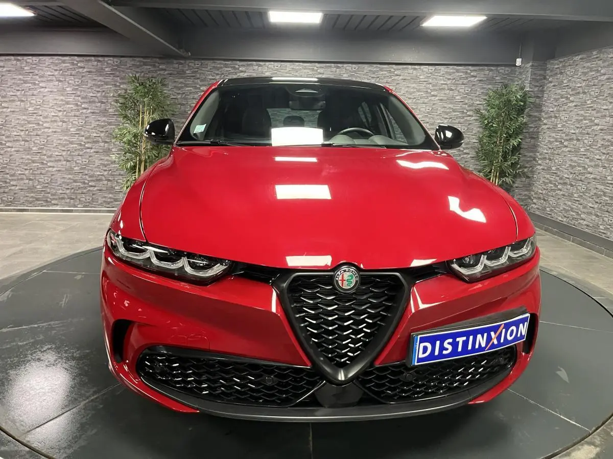 Vue frontale d'une Alfa Romeo Tonale rouge avec calandre noire en V et phares LED distinctifs dans un showroom.