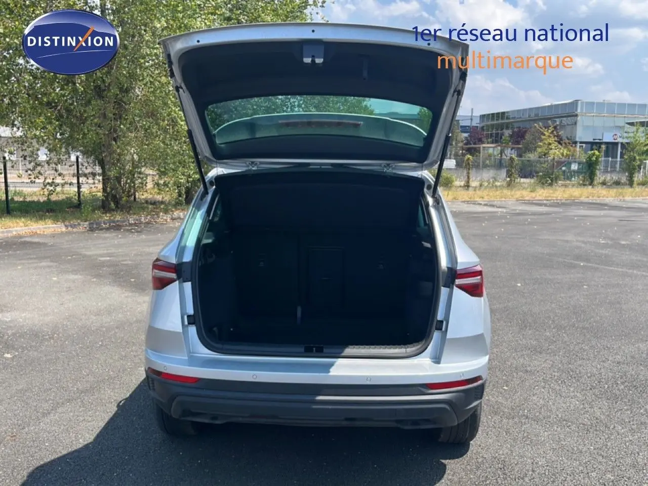 Vue arrière d'un Skoda Karoq 1.5 TSI 150CH DSG7 en Reflex Silver Metal avec coffre ouvert sur un parking extérieur.