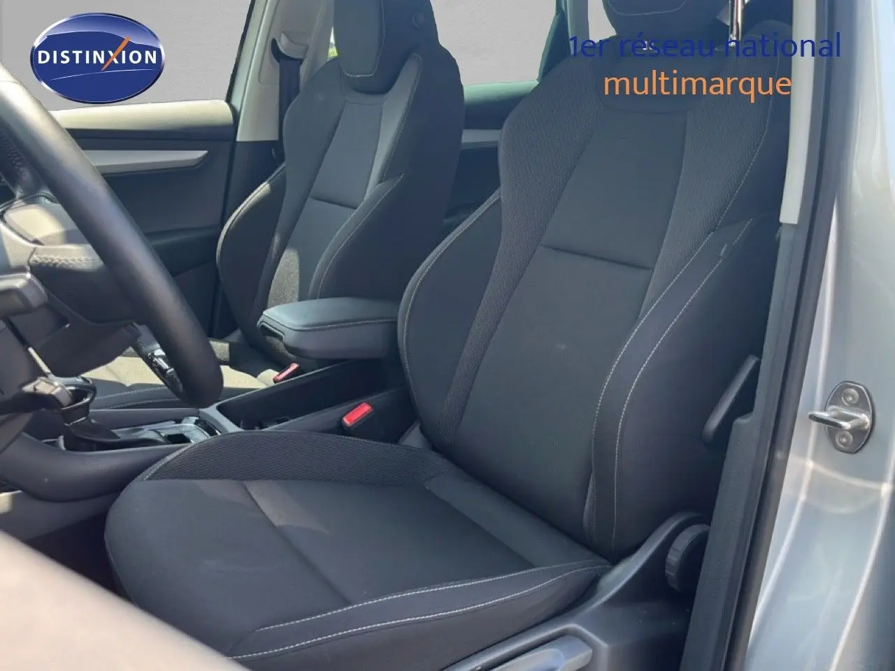 Vue intérieure côté conducteur du Skoda Karoq 1.5 TSI 150ch en tissu noir avec accoudoir central, porte ouverte couleur argent.