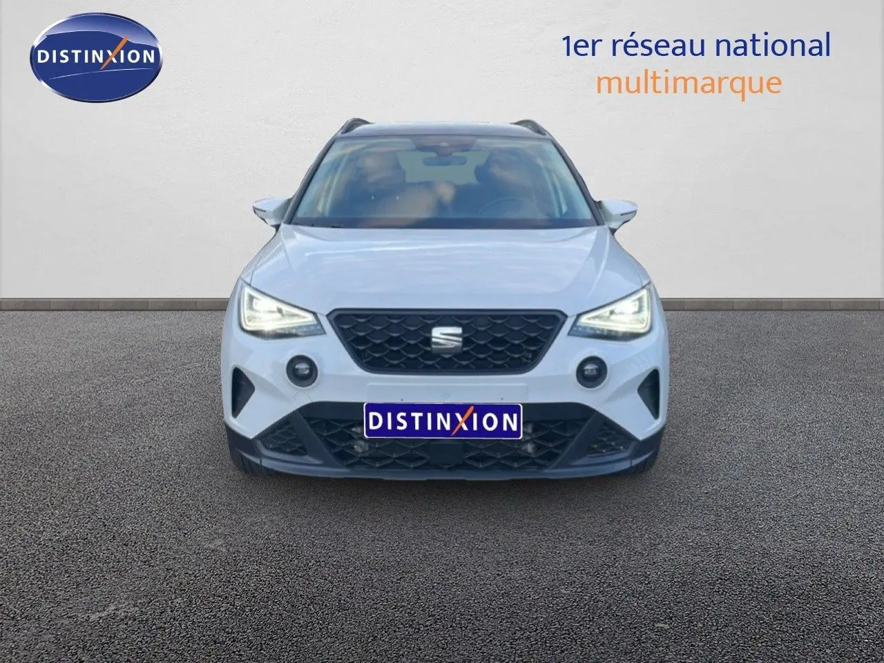 Vue frontale d'un SEAT Arona blanc avec toit gris, phares allumés et calandre noire distinctive.