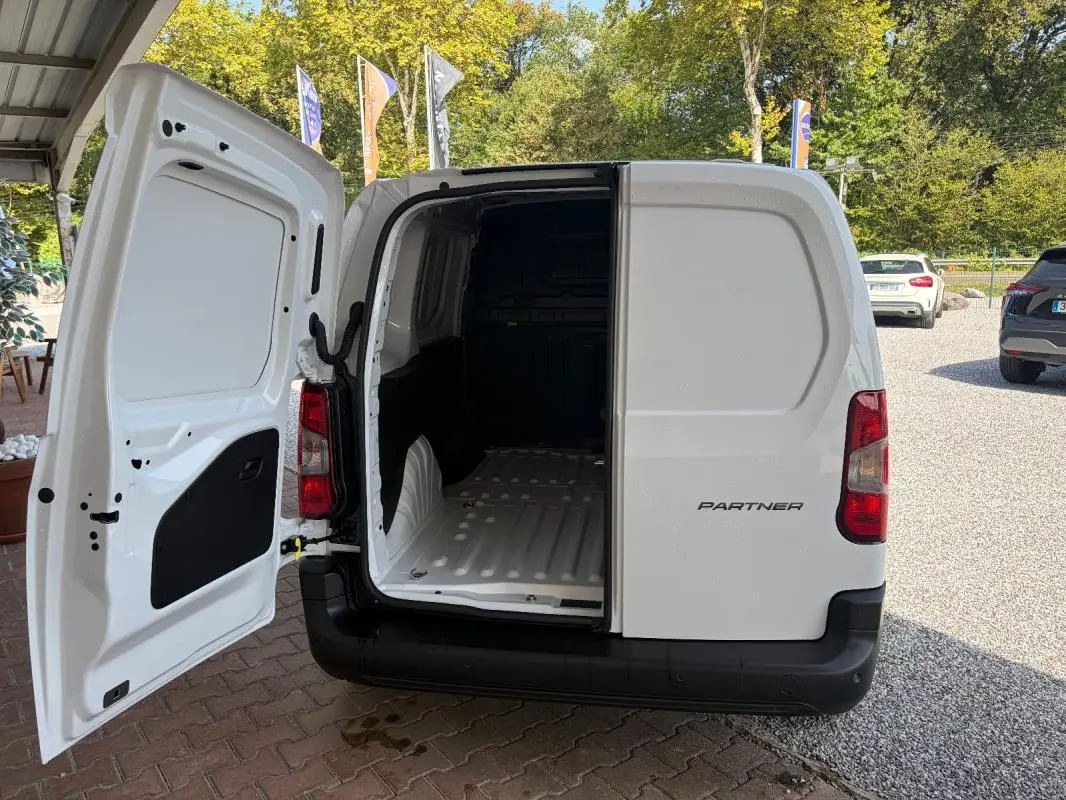 Vue arrière d’un Peugeot Partner blanc 2026 avec porte arrière gauche ouverte montrant l’espace de chargement vide.