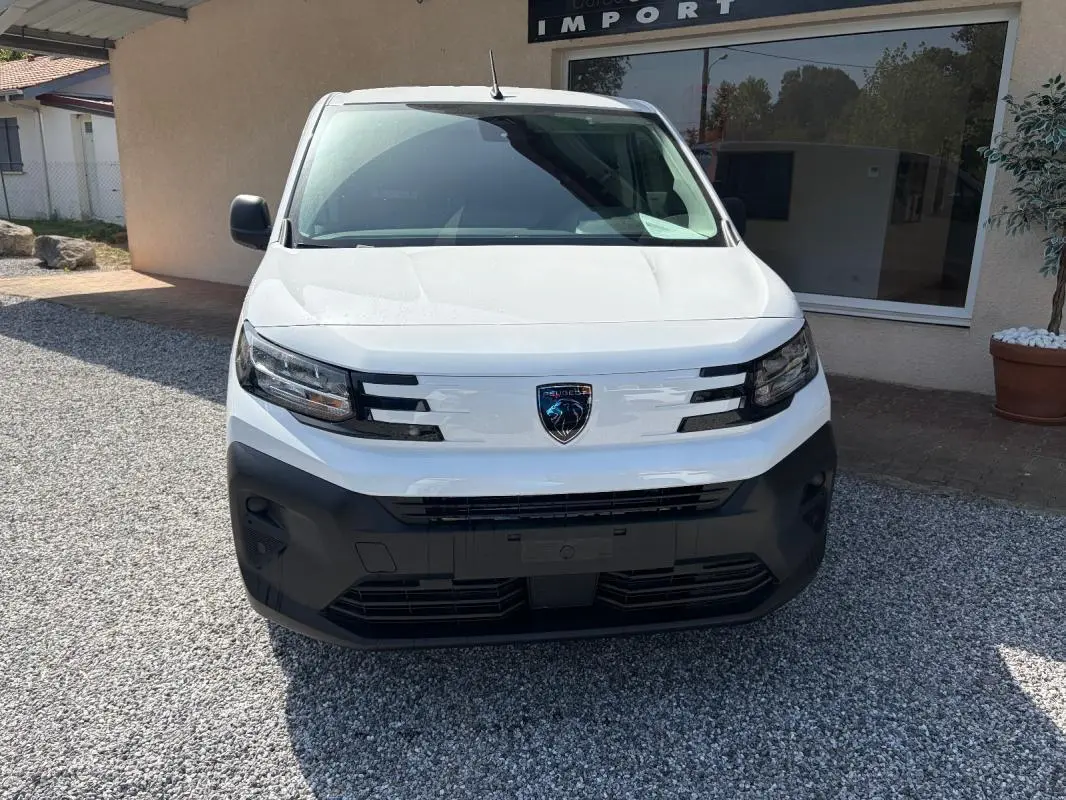 Vue frontale du Peugeot Partner blanc avec calandre noire et logo Peugeot visible, stationné sur gravier.