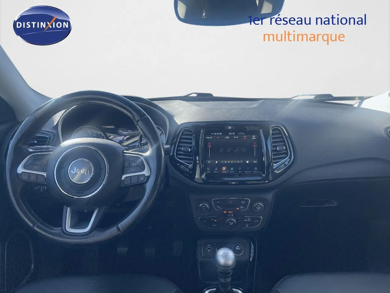 Vue intérieure du tableau de bord et volant du Jeep Compass gris foncé, avec écran tactile et levier de vitesse manuel visible.