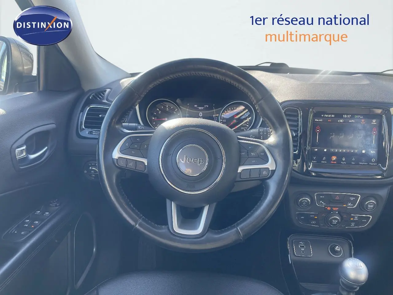 Vue intérieure centrée sur le volant Jeep Compass gris foncé, tableau de bord et console avec écran tactile visible.
