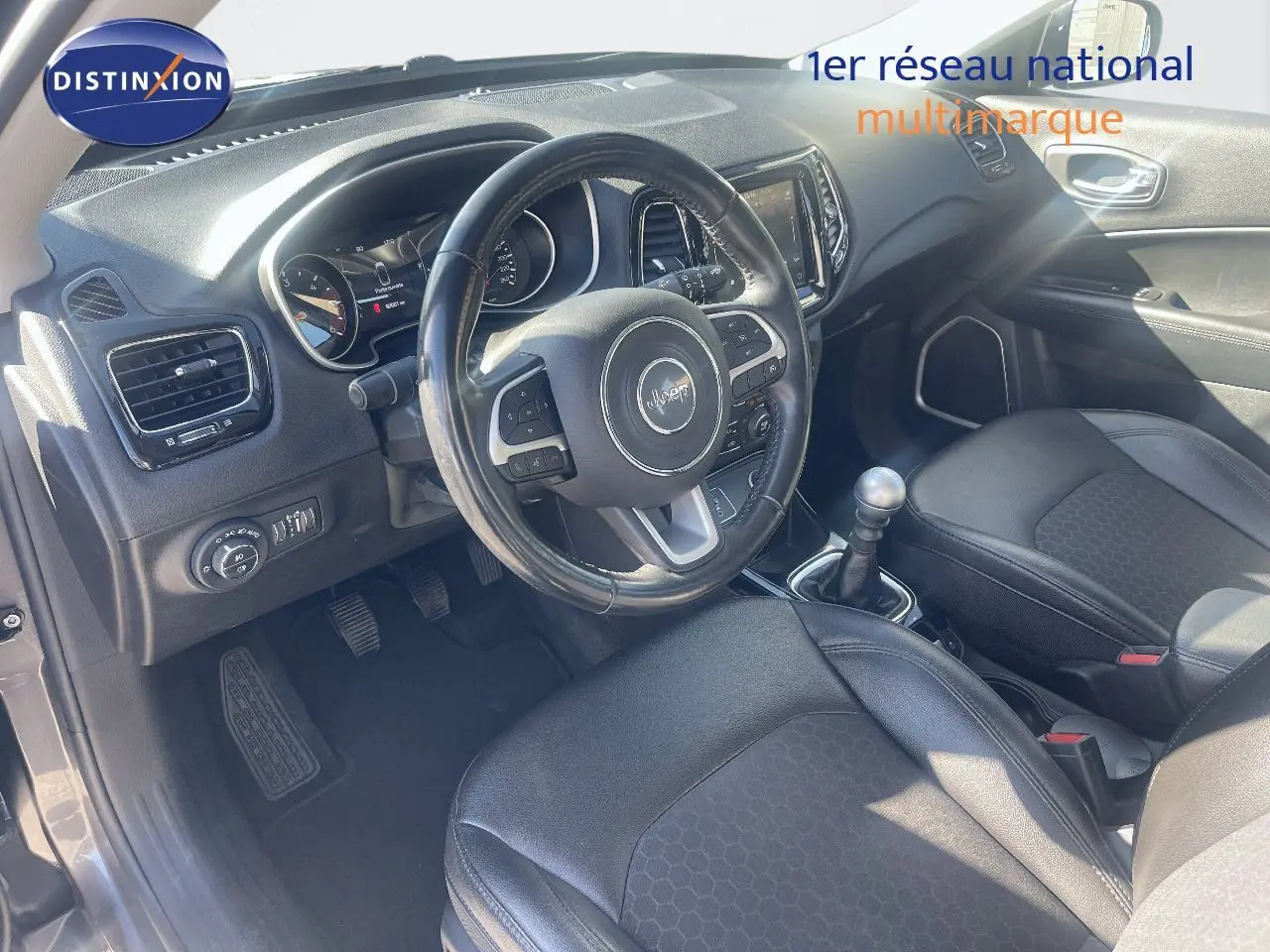 Vue intérieure côté conducteur du Jeep Compass gris foncé, mettant en valeur le volant multifonction et la boîte manuelle.