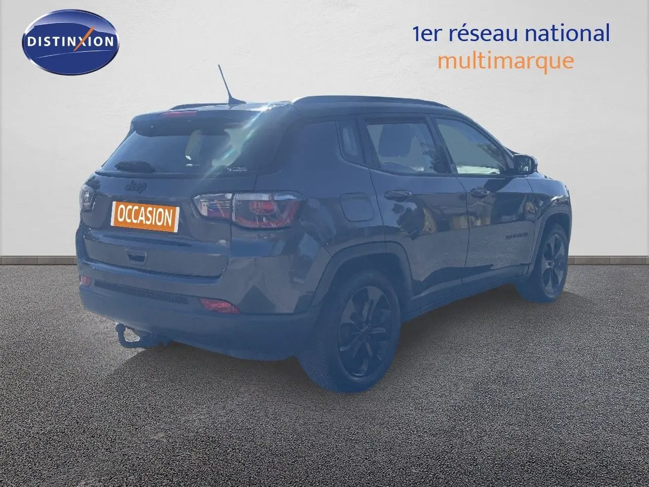 Jeep Compass gris foncé en 3/4 arrière droit, version Brooklyn Edition avec jantes noires et attelage visible.