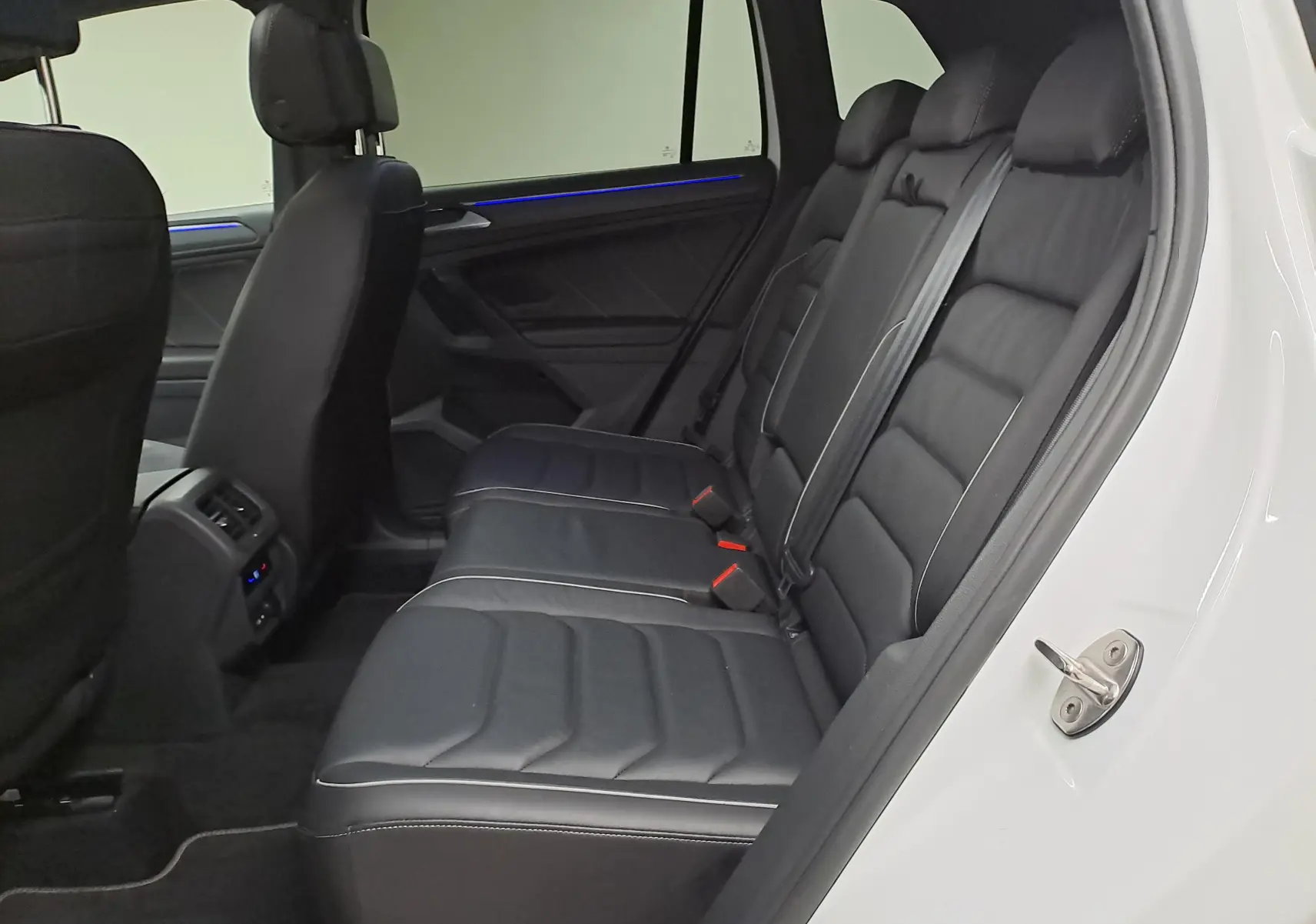 Vue intérieure côté droit des sièges arrière en cuir noir du Volkswagen Tiguan blanc nacré 2023, avec éclairage d'ambiance bleu.