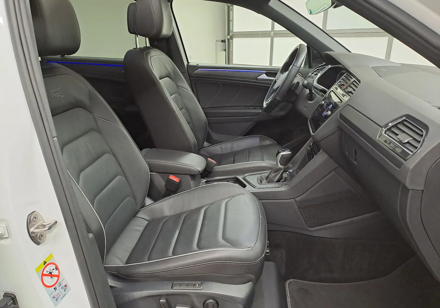 Vue intérieure côté conducteur du Volkswagen Tiguan blanc nacré 2023, sièges cuir noirs et tableau de bord moderne.