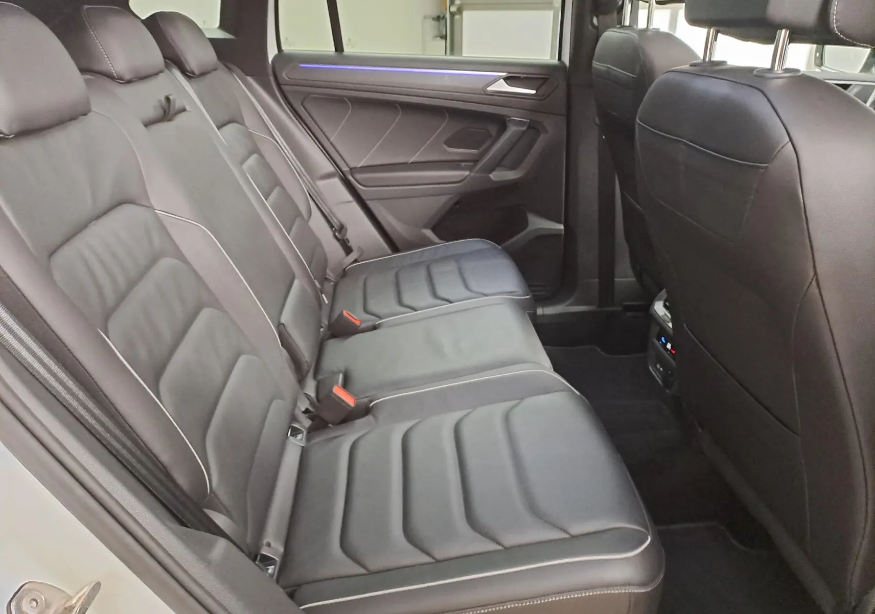 Vue intérieure côté gauche des sièges arrière en cuir noir avec surpiqûres blanches du Volkswagen Tiguan blanc nacré 2023.