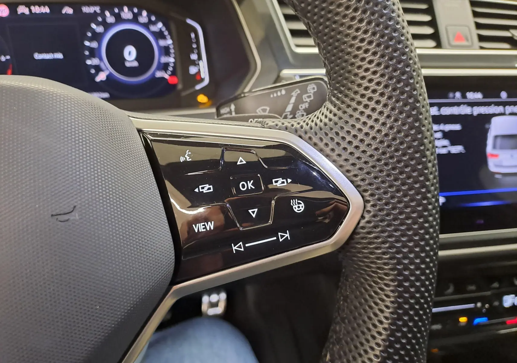 Gros plan sur le volant perforé du Volkswagen Tiguan 2023, avec commandes multifonctions noires et tableau de bord numérique en arrière-plan.