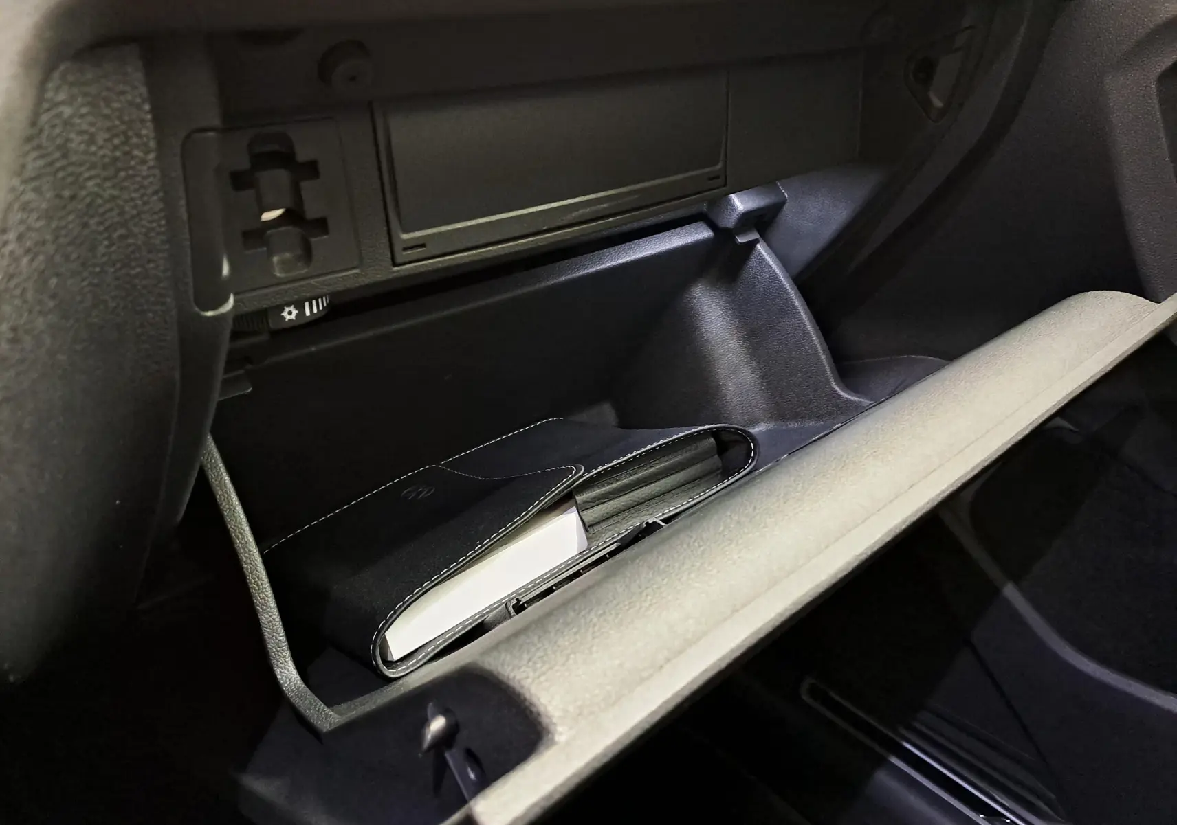 Gros plan sur la boîte à gants ouverte du Volkswagen Tiguan, montrant un carnet noir à l'intérieur, intérieur noir.