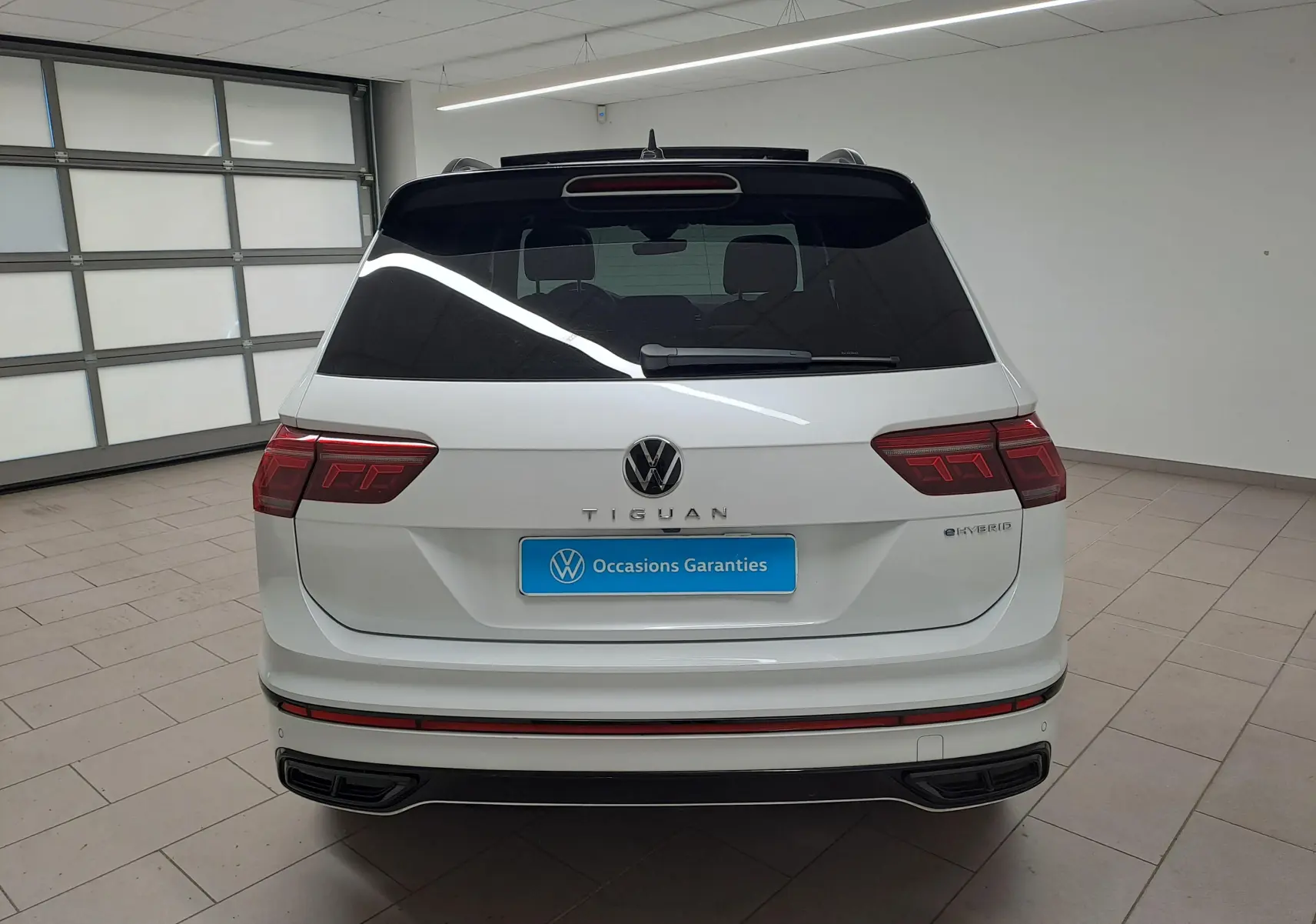 Vue arrière d'un Volkswagen Tiguan blanc nacré eHybrid 2023 avec logo et feux LED distinctifs en intérieur showroom.