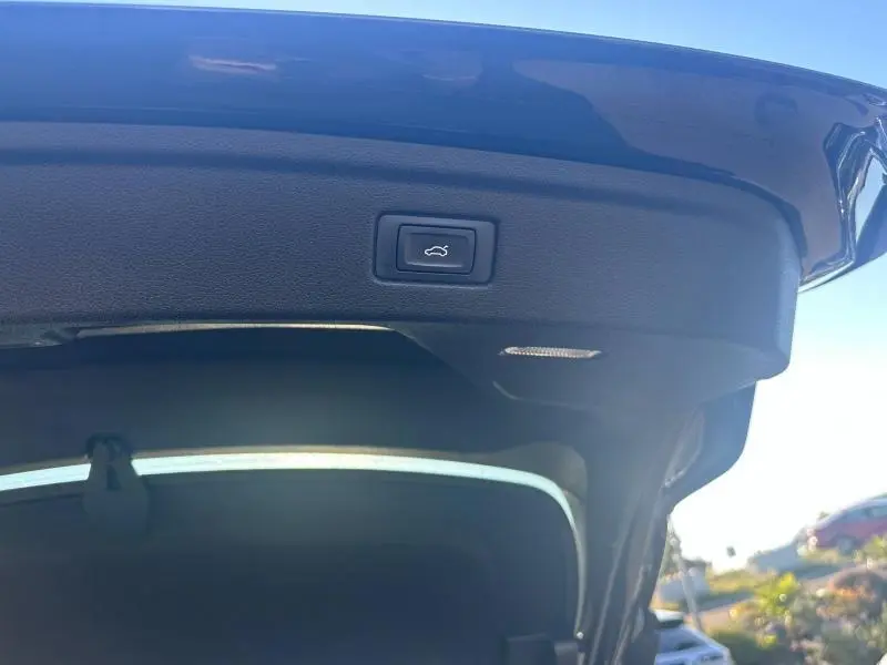 Bouton d'ouverture électrique du hayon sur la partie intérieure du coffre d'une Audi A5 Sportback noire vue de dessous.