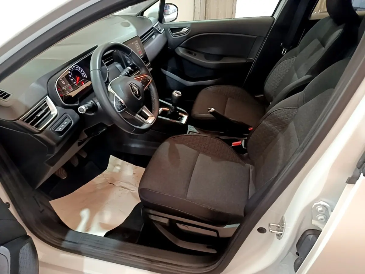 Vue intérieure côté conducteur de la Renault Clio Business blanche, montrant les sièges noirs et le volant multifonctions.