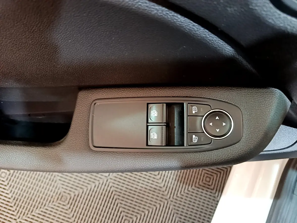 Vue rapprochée des commandes de lève-vitres et réglage des rétroviseurs côté conducteur d’une Renault Clio blanche.