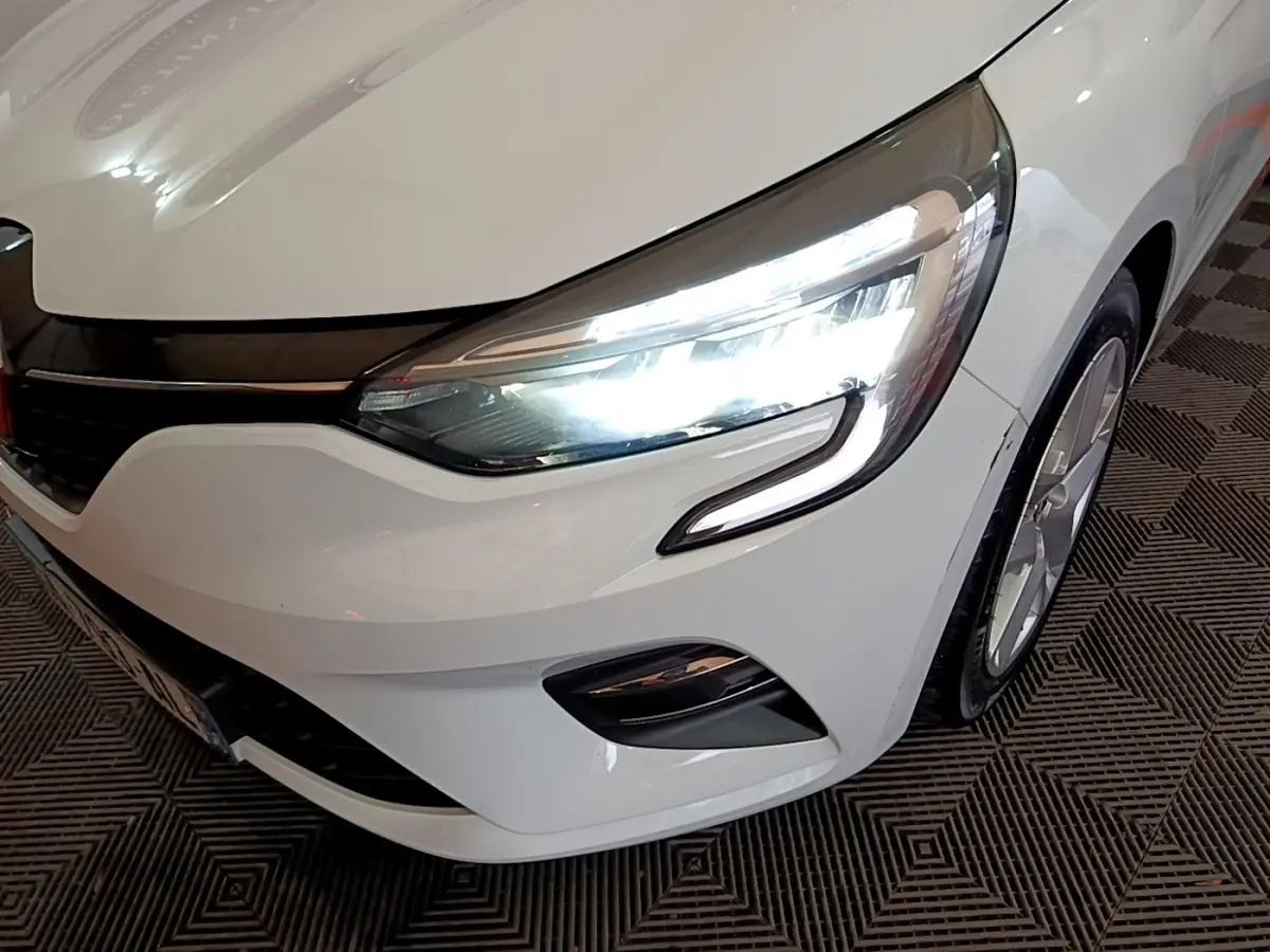 Gros plan sur l'avant droit d'une Renault Clio blanche 2021 avec phares LED allumés et jante visible.