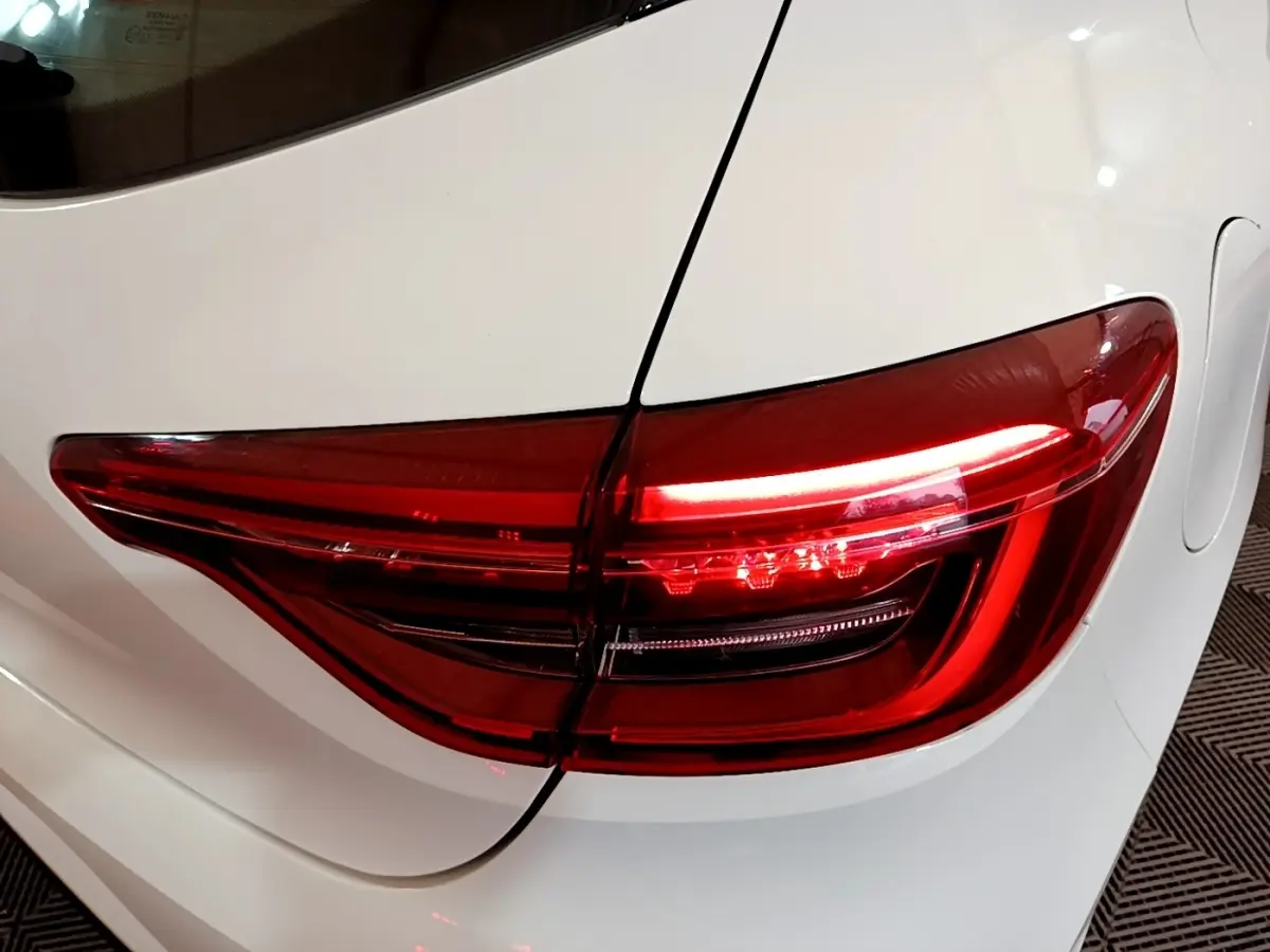 Feu arrière droit allumé sur Renault Clio Business blanche, vue rapprochée du coffre et de la portière arrière.