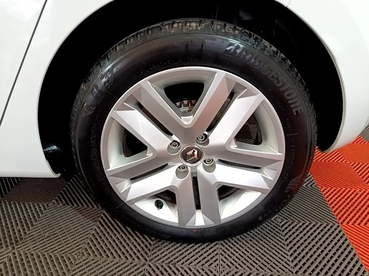 Gros plan sur la roue avant droite d’une Renault Clio blanche, jante alliage à cinq branches doubles, logo Renault au centre.