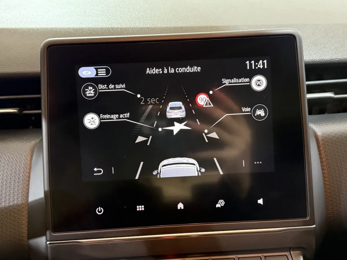 Écran tactile central de la Renault Clio Business blanc, affichant les aides à la conduite avec alertes et distances.