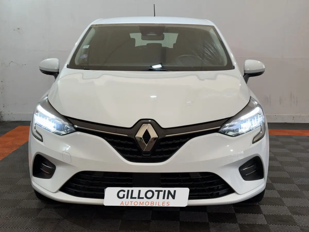 Vue frontale d'une Renault Clio Business SCe 75 blanche avec phares LED allumés et calandre noire distinctive.