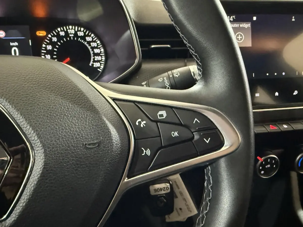 Gros plan sur le volant multifonction en cuir noir de la Renault Clio Business, avec tableau de bord et écran tactile en arrière-plan.