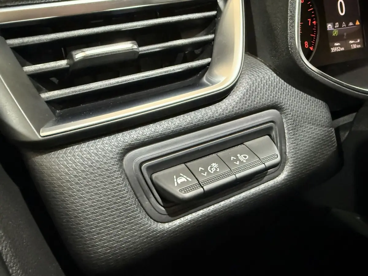 Gros plan sur les commandes d'assistance et réglage des phares à gauche du tableau de bord d'une Renault Clio Business blanche.