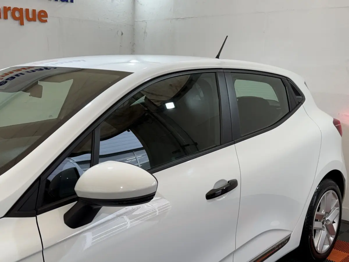 Vue latérale gauche d'une Renault Clio Business SCe 75 blanche, avec rétroviseur et poignées noires contrastantes.