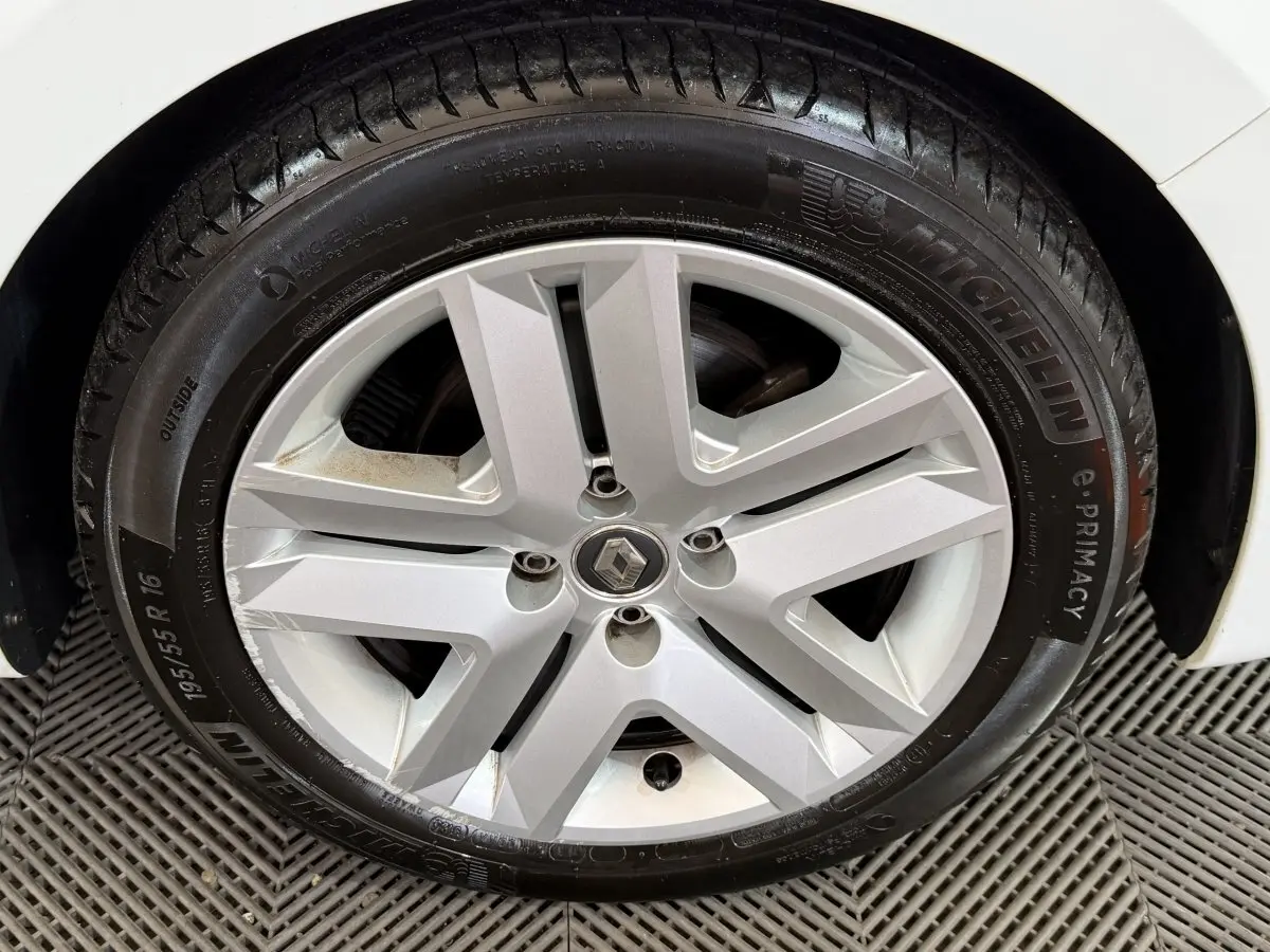 Gros plan sur la roue avant droite d’une Renault Clio blanche, jante alliage argentée à cinq branches doubles.