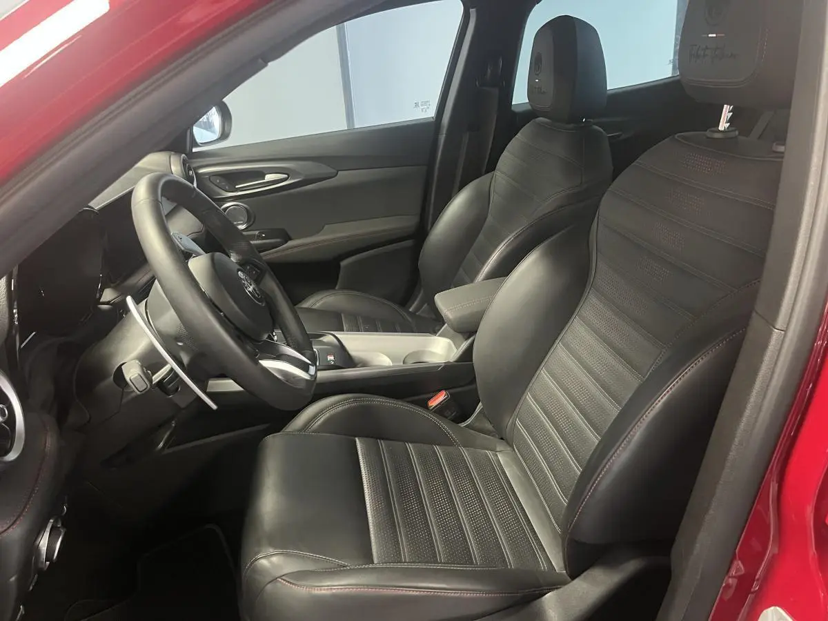 Vue intérieure côté conducteur de l'Alfa Romeo Tonale rouge 2024 avec sellerie cuir noir et surpiqûres rouges.