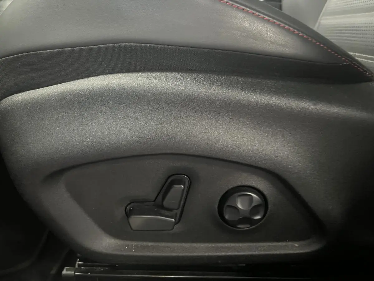 Gros plan sur les commandes électriques de réglage du siège en cuir noir avec surpiqûres rouges de l'Alfa Romeo Tonale rouge.