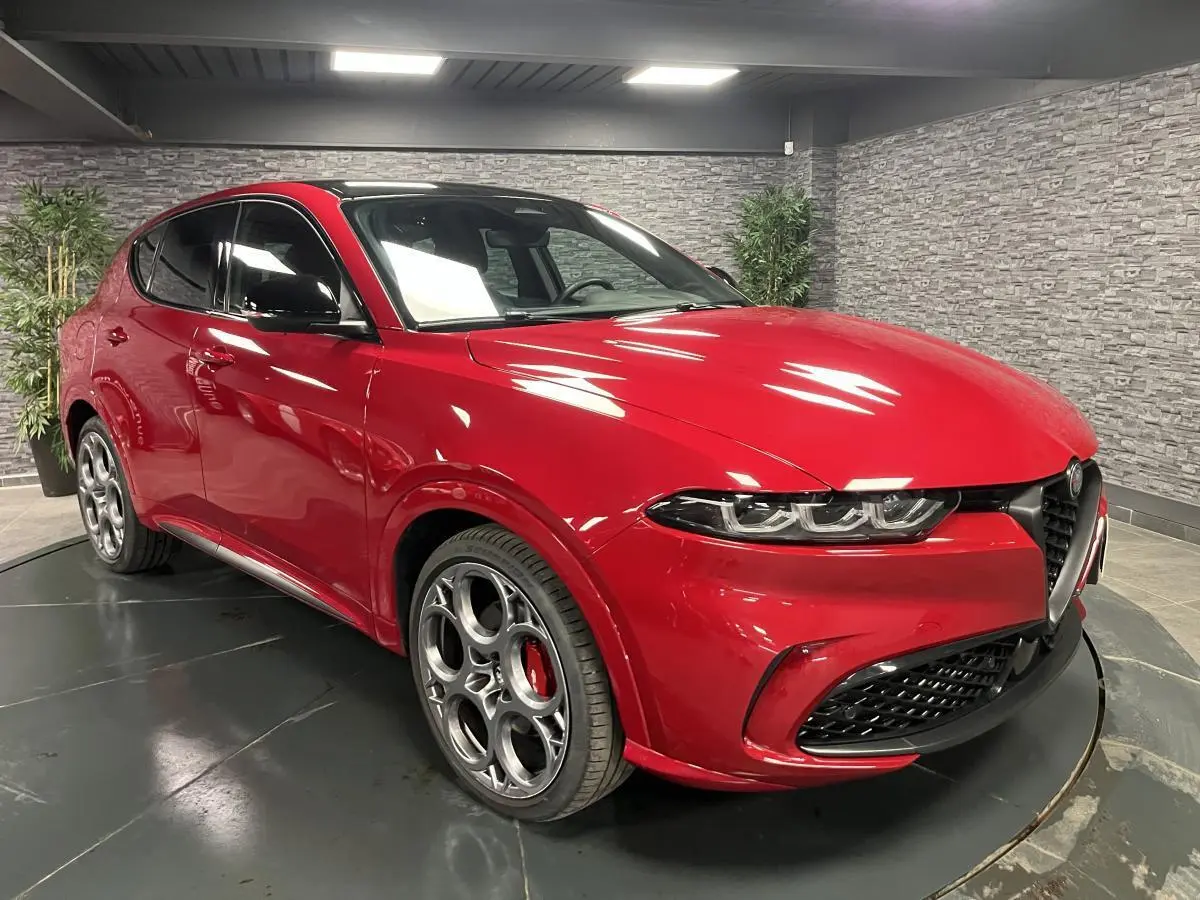 Vue 3/4 avant gauche de l'Alfa Romeo Tonale rouge avec jantes 20 pouces et toit noir en intérieur showroom.