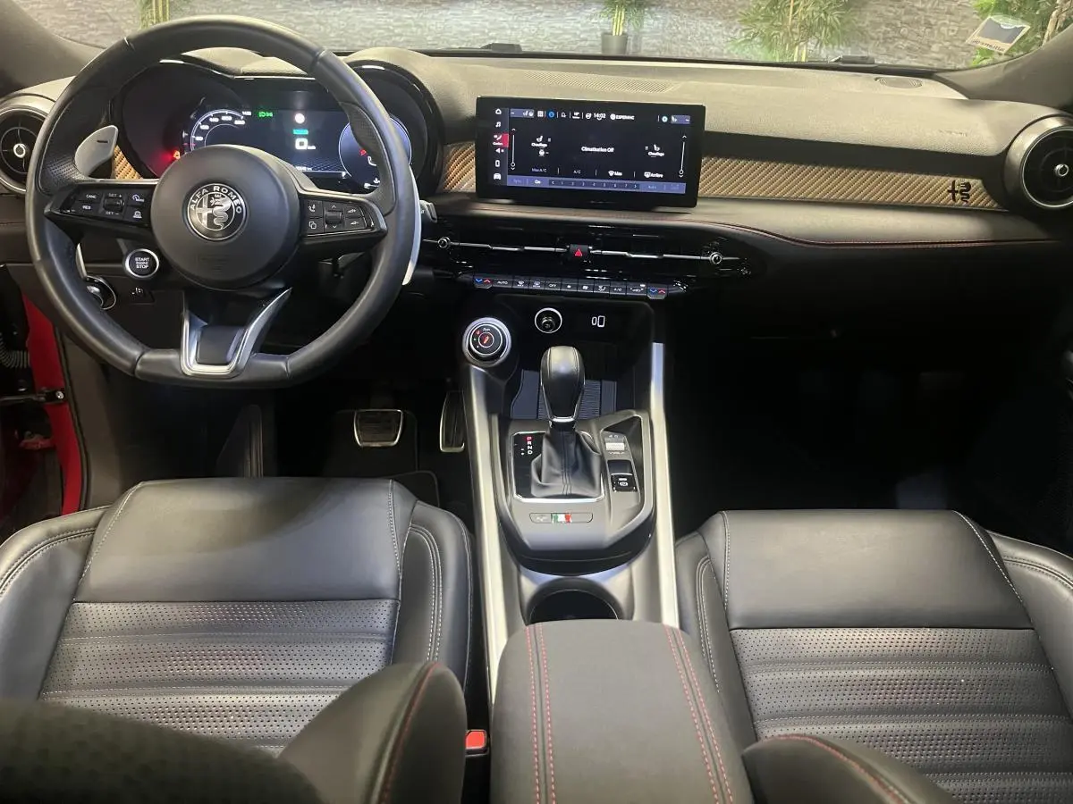 Vue intérieure avant de l'Alfa Romeo Tonale 2024, volant sport cuir noir, écran tactile et inserts carbone sur tableau de bord.